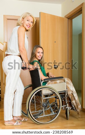 Smiling elderly mother helping handicapped girl to enter the apartment. Focus on girl