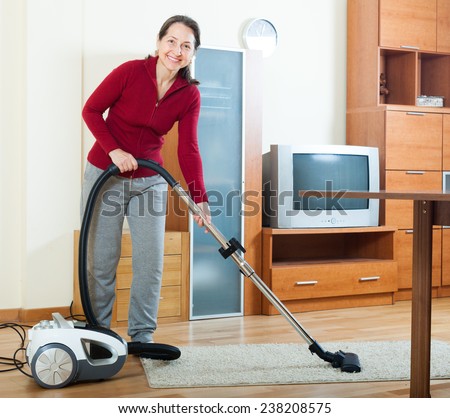 Happy mature woman cleaning with vacuum cleaner on parquet floor