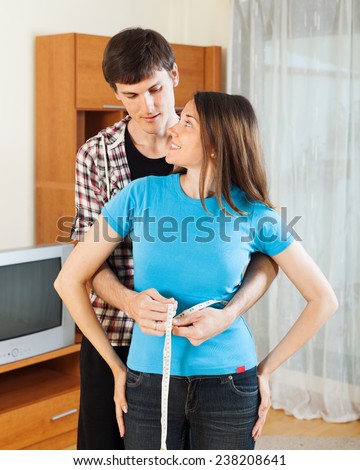 Man measuring waist of girl with measuring tape at home