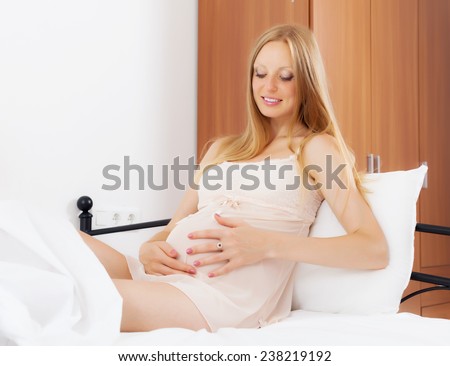 Ordinary pregnant woman wearing nightgown sitting in her bed at home