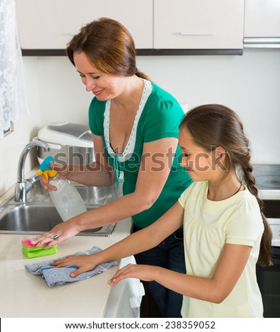 Smiling schoolgirl helping mother dusting furniture indoor. Focus on girl