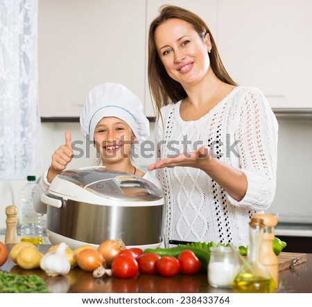 Happy mother and little daughter 9-10 years old using multicooker at kitchen