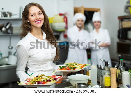 Team of chefs and young beautiful waiter in restaurant kitchen