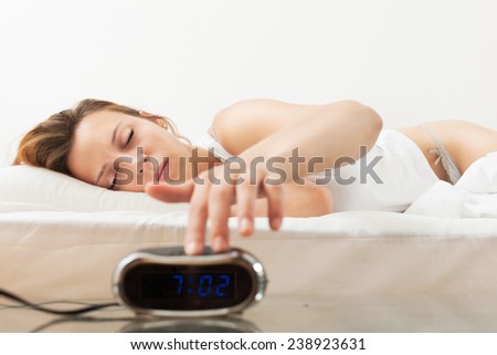 Sleeping young woman in the morning switching off the alarm clock in bad