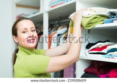 Smiling middle-aged female customer choosing apparel on shelves at store