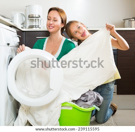 Home family laundry. Mother with playful daughter loading clothes into washing machine in kitchen