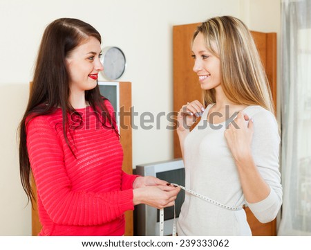 Young woman measuring  waist of happy girlfriend with measuring tape at home