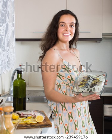 Smiling housewife putting pieces of lemon in fish at home kitchen