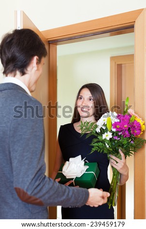 Young woman giving flowers and gift to guy near home  door
