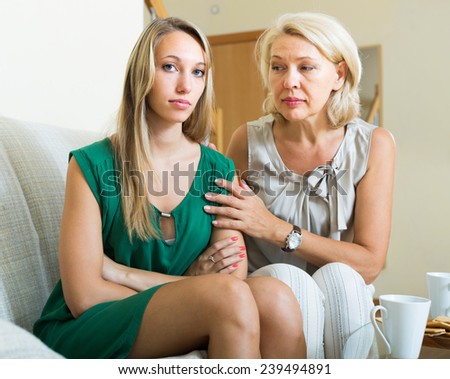 Mature mother comforting crying adult daughter at home. Focus on young