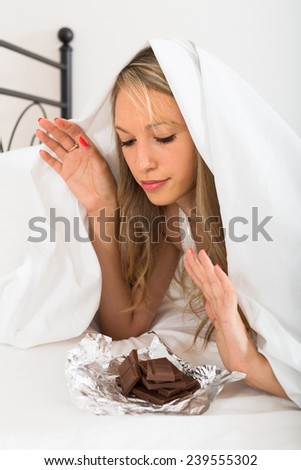 Long-haired blonde young woman eating chocolate in bed