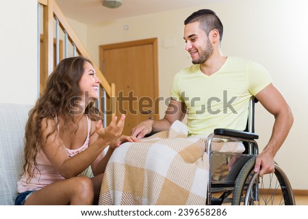 Handsome  handicapped man  in wheelchair and his  girlfriend having conversation in room