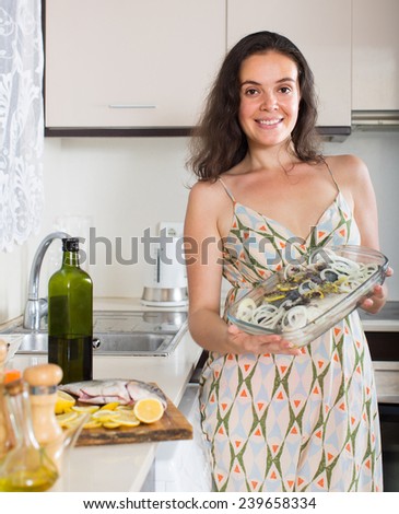 Smiling  girl with raw fish on roasting pan at home kitchen