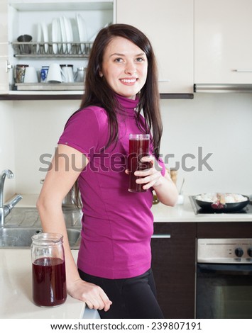 Smiling woman drinking  fruit-drink or juice from glass at home kitchen