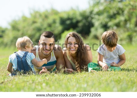 Portrait of happy smiling young parents with children in grass at park. Focus on man