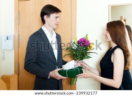 Smiling man giving flowers and gift to woman at home