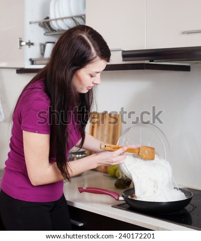 Woman cooking chinese noodles  in skillet at home kitchen