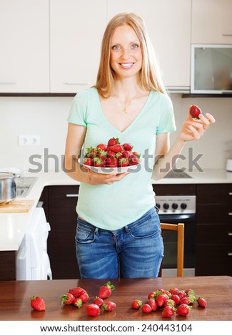Happy blonde girl holding  heap of strawberries at home kitche