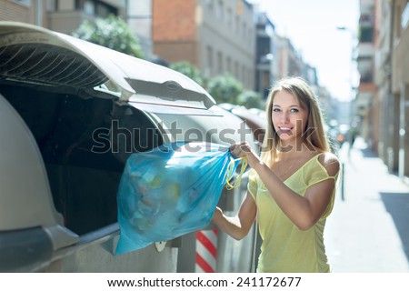 Smiling girl with rubbish near refuse collection container