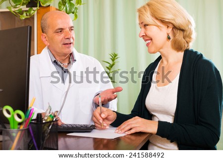 Male doctor talking with smiling mature patient in clinic office