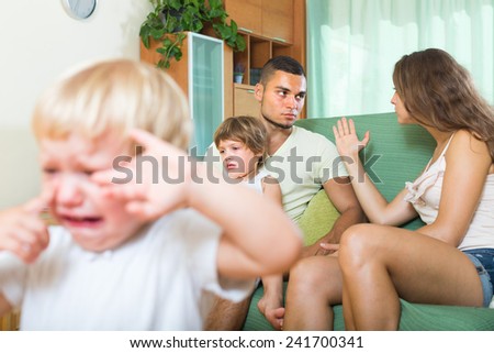 Young family with two little daughters having quarrel in the living room. Focus on man
