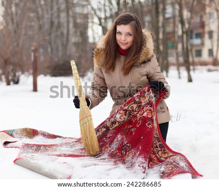 Smiling woman cleans red carpet with snow in winter day outdoor