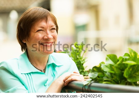 Female pensioner resting at balcony with flowers and smiling