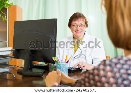 Elderly doctor communicates with patient sitting at computer