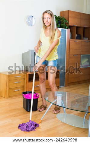 Blonde  long-haired woman washing parquet floor with mop at home