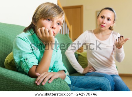 Angry mother scolding naughty teenage son in home interior. Focus on boy