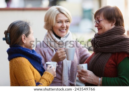Smiling mature female in warm clothes having cup of hot tea on terrace