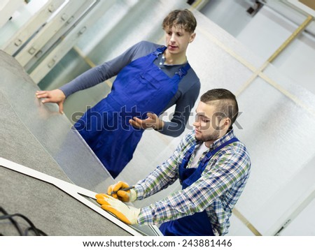 Two careful  males cutting glass for windows at workshop