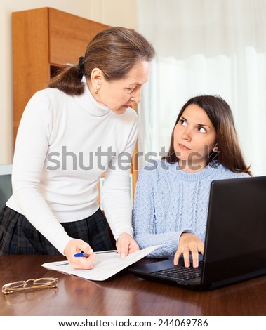 serious    mature woman and teenager daughter at table with laptop in home or office