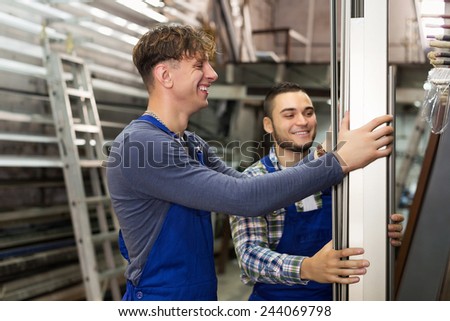 Two smiling production workmen in uniform with different PVC window profiles