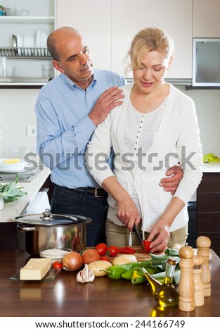 Loving elderly senior and mature woman cooking vegetables together in domestic kitchen