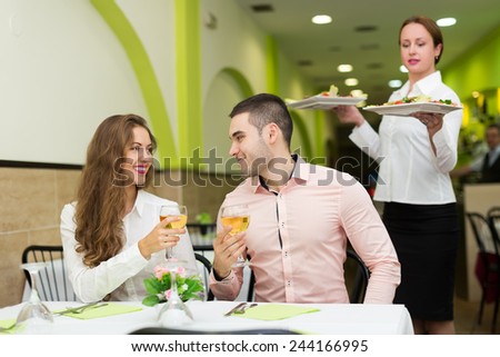 Young couple at table and waitress with plates in restaurant