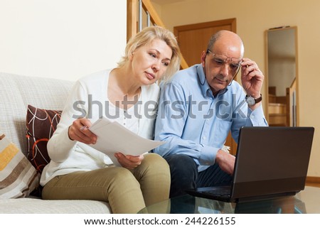 Serious mature man and woman reading finance documents in home interior
