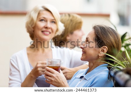 Smiling elderly female colleagues having lunch break at patio and drinking tea