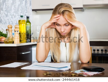 Young sad blonde housewife filling in utility payments bills at home