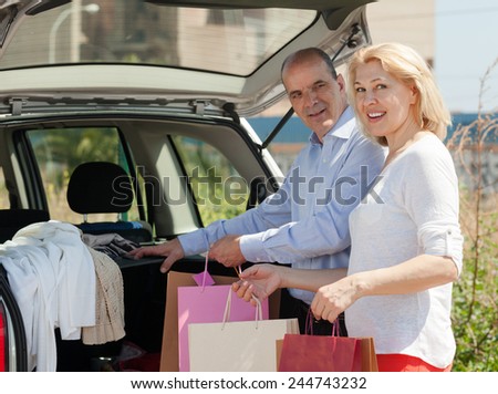Happy mature couple with purchases after shopping staying near opened boot