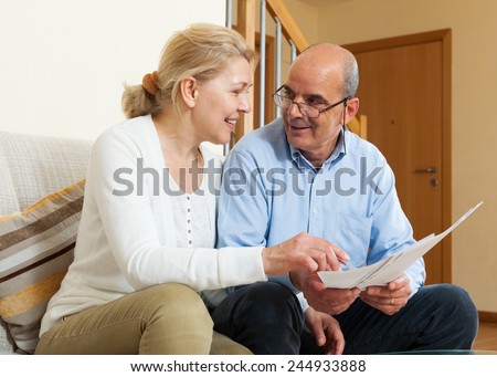 Smiling elderly couple with financial documents on sofa in home interior