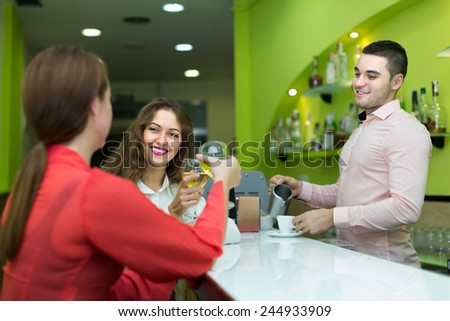 Smiling young bartender and two women with wine at bar. Focus on girl
