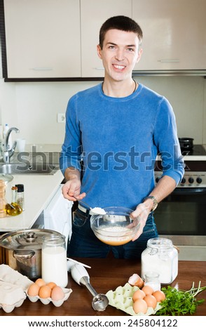 Smiling european man cooking omelet with flour in home kitchen