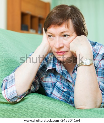 Stressed woman pensioner laying on her elbows and thinking  on couch