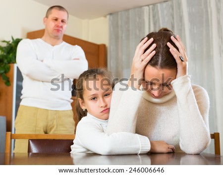 Daughter comforting sad mother in room at home and angry father