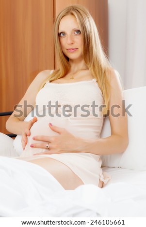 Ordinary pregnant woman wearing nightgown sitting in  bed