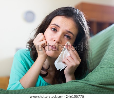 Unhappy young long-haired woman crying on couch at home
