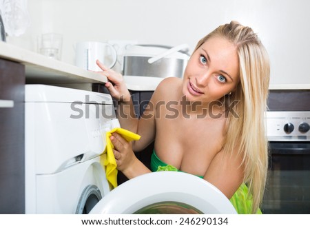 Blonde young woman cleaning washing machine at home kitchen