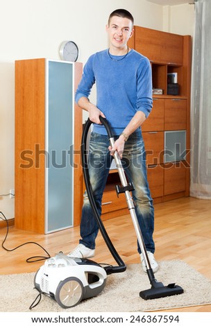 Ordinary guy  cleaning with vacuum cleaner on parquet floor in home