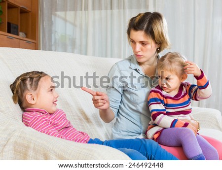 Little girl watching angry mom showing finger to older sister indoor
